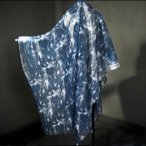 May include: A draped, sheer fabric with a tie-dye effect in blue and white. The fabric is displayed over a rod, highlighting its texture and pattern. The item appears to be a shawl or wrap, ideal for adding an artistic touch to any ensemble.