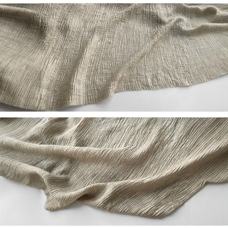 May include: Close-up of a beige fabric with a textured, crinkled appearance. The fabric is draped, with visible folds and subtle variations in tone. The material appears soft and lightweight, suitable for clothing or home decor.