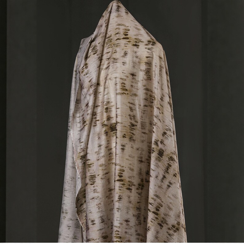 Puede incluir: Una tela drapeada en tonos neutros, con un patr&oacute;n de pinceladas marr&oacute;n oscuro y verde oliva. La tela est&aacute; drapeada sobre una forma invisible, creando pliegues y sombras suaves. El textil parece ligero y fluido, adecuado para ropa o decoraci&oacute;n.