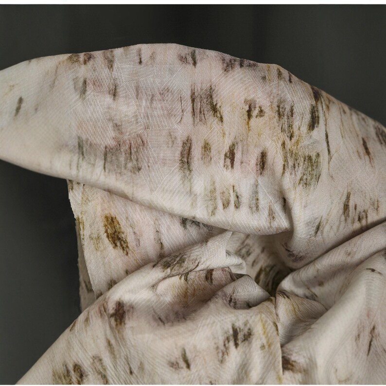 Puede incluir: Primer plano de una tela color crema con un patr&oacute;n texturizado. La tela presenta un dise&ntilde;o irregular en tonos marrones y verdes, creando un aspecto natural y org&aacute;nico. La tela est&aacute; doblada, mostrando la textura y la ca&iacute;da del material.