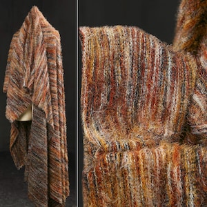 Op de afbeelding: Een getextureerde, veelkleurige sjaal in tinten bruin, oranje en zwart. De stof lijkt een zacht, fuzzy materiaal te zijn met een diagonaal gestreept patroon. De sjaal is over een vorm gedrapeerd, wat de vorm en de val ervan laat zien.