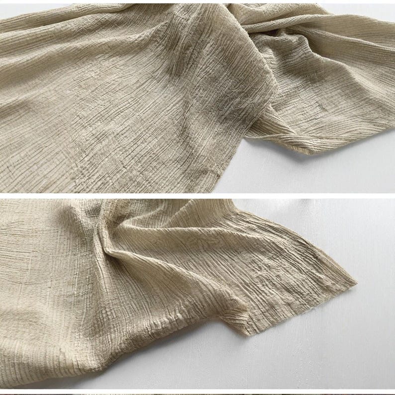 Puede incluir: Primer plano de una tela beige con una apariencia texturizada y arrugada. La tela est&aacute; drapeada y doblada, mostrando su superficie detallada. El color neutro y la textura sugieren un enfoque en materiales naturales y una est&eacute;tica minimalista.