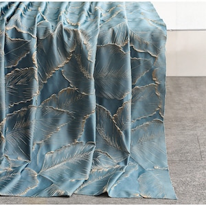 Könnte beinhalten: Ein drapierter Vorhang in einem sanften Blauton mit einem sich wiederholenden Muster aus goldfarbenen, federartigen Designs. Der Stoff hat einen subtilen Glanz, der dem Design Tiefe verleiht. Der Vorhang ist gefaltet und zeigt die komplizierten Details des Musters.