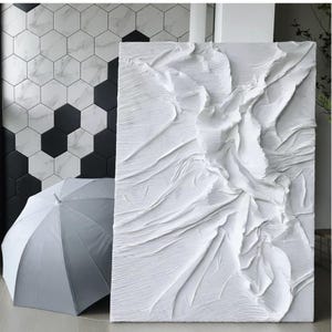 May include: A large, textured white abstract art piece with a rippled surface. A white umbrella is open and leaning against the wall. The wall has a black and white geometric tile pattern.