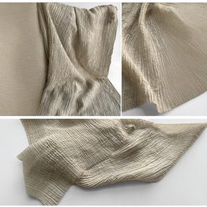 May include: Close-up shots of a beige fabric with a textured, crinkled appearance. The fabric is draped and folded, showing its rippled surface. The lighting highlights the subtle colour and texture variations, creating a soft, flowing effect.