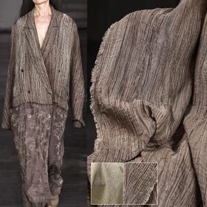 May include: A brown, textured blazer and matching pants. The blazer has a double-breasted design with two visible buttons and pockets. The pants have a floral pattern. The fabric has a crinkled appearance.