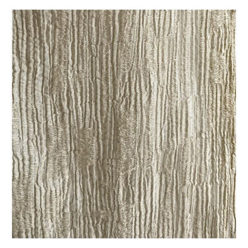 Puede incluir: Primer plano de una tela texturizada de color blanquecino con l&iacute;neas verticales onduladas. La tela tiene un aspecto ligeramente rugoso, con sutiles variaciones de tono y textura. El efecto general es suave y natural.