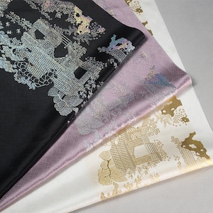 Könnte beinhalten: Drei Seidenstoffe in Schwarz, Lavendel und Weiß, jeweils mit einem verzierten, metallischen Architekturdesign. Der schwarze Stoff hat ein silbernes Design, der Lavendel hat ein schimmerndes silbernes Design und der weiße Stoff hat ein goldenes Design.