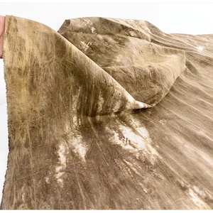 May include: A piece of fabric with a textured, tie-dye pattern in shades of brown and white. The fabric is folded, revealing the layered texture and color variations. The material appears to be natural, possibly linen or cotton.