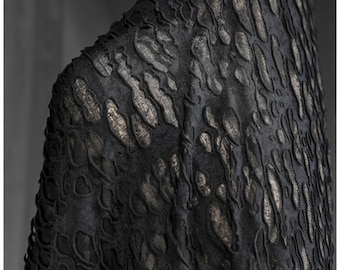 May include: Close-up of a black fabric with a textured pattern. The pattern features raised, organic shapes in a darker tone, with metallic gold accents. The fabric appears to be draped, suggesting it could be part of a garment or textile.