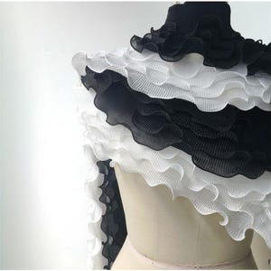 以下が含まれることがあります： マネキンの上に黒と白のフリル付きの衣服。 衣服は、黒と白のフリルの交互のバンドを特徴とし、重ね着効果を生み出しています。 フリルは波状の質感で、衣服は軽量の生地で作られているようです。