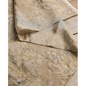 Può includere: Primo piano di un tessuto piegato con un motivo botanico. Il tessuto ha una palette di colori tenui di beige, grigio e sfumature di oro. Il design presenta delicati motivi di foglie e fiori, creando un aspetto strutturato.