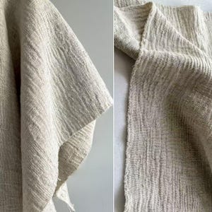 May include: Close-up of a textured, off-white fabric. The fabric has a woven appearance with a slightly crinkled texture. The image shows the edge of the fabric, revealing a raw, unfinished edge. The fabric appears to be a natural fiber, possibly linen or cotton.