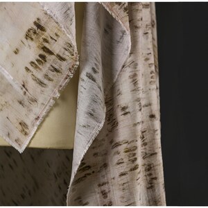 Puede incluir: Bufanda color crema con un estampado de corteza de abedul en tonos marrones y verdes. La bufanda tiene un borde con flecos y est&aacute; drapeada sobre un maniqu&iacute;. La tela parece ligera y fluida.