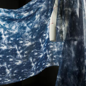 May include: A draped fabric featuring a tie-dye design in blue and white hues. The material is patterned with a marbled effect, with deep indigo sections contrasting with lighter, almost white, areas. A dress form is partially visible.