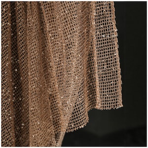 May include: Close-up of a brown, net-like fabric with a grid pattern. The fabric has a slightly textured appearance and is speckled with small, light-colored details. The edges of the fabric are visible, showing the woven construction.