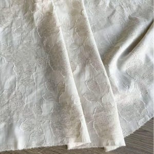 May include: A white ceramic mug with a black handle and the text "But First, Coffee" in a bold, black font. The mug is on a wooden surface. The mug is approximately 10 cm tall.