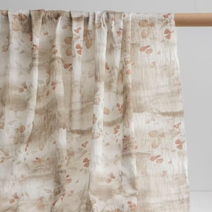 May include: A draped fabric with a natural, organic aesthetic. The textile features a cream-coloured base with brown and peach-coloured botanical patterns and horizontal stripes. The fabric is hanging from a wooden rod, showcasing its flowing texture.