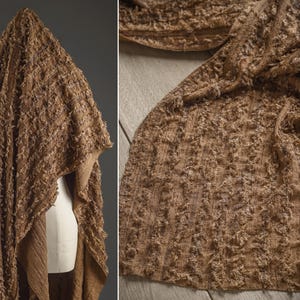 Peut inclure: Un tissu marron texturé, peut-être un châle ou une écharpe, drapé sur un mannequin et étalé sur une surface en bois. Le tissu a une texture en relief et une teinte chaude et terreuse.