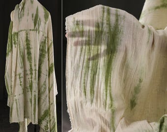 Puede incluir: Tela de color crema con rayas verticales verdes teñidas con la técnica tie-dye. La tela está drapeada, mostrando su textura y transparencia. Se muestra sobre un maniquí y en primer plano, lo que sugiere que es ligera.