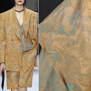 May include: A tan two-piece suit, comprising a double-breasted blazer and shorts. The fabric displays a swirling, abstract pattern in teal and brown. The material has a textured finish, creating a unique visual appeal.