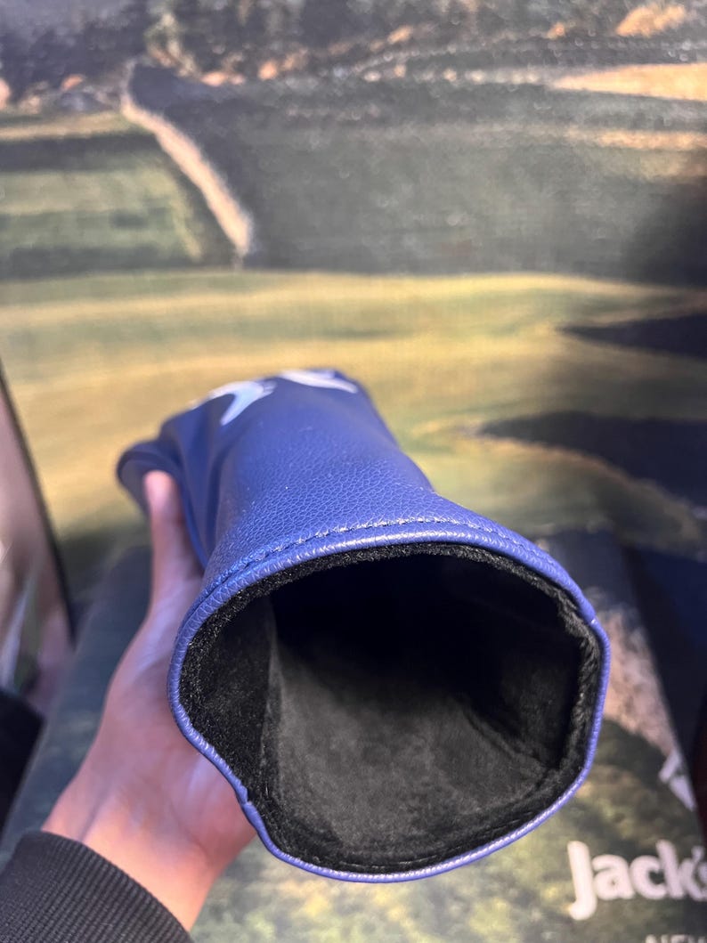 May include: A blue golf club head cover with a star design. The cover is made of a smooth material and has a black interior lining. The cover is designed to protect the golf club head.