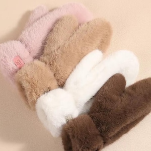 Puede incluir: Un conjunto de mitones de piel sintética en tonos rosa, beige, blanco y marrón. Cada mitón tiene una textura suave y afelpada y un puño en la muñeca. Los mitones están dispuestos en un patrón en capas, mostrando sus variados colores y texturas.