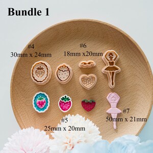 May include: A collection of cookie cutters in various shapes, including strawberries, hearts, and a ballerina. The cutters are in shades of pink, white, and brown. The text "Bundle 1" is at the top. Measurements are provided in millimeters.