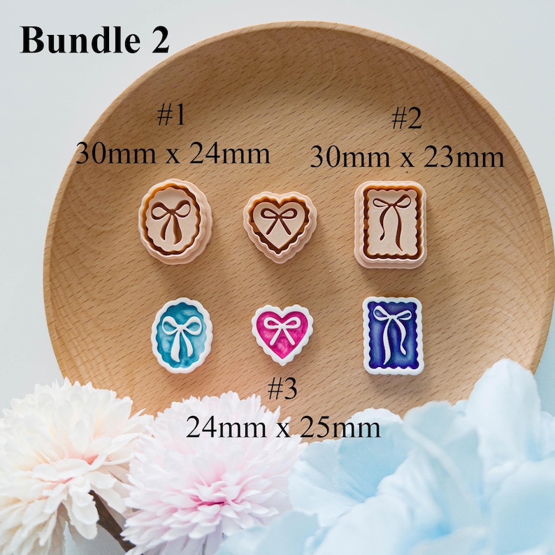May include: A collection of six decorative stamps in various shapes, including round, heart, and square, each featuring a bow design. The stamps are in shades of brown, pink, blue, and white. Measurements are provided in millimeters.