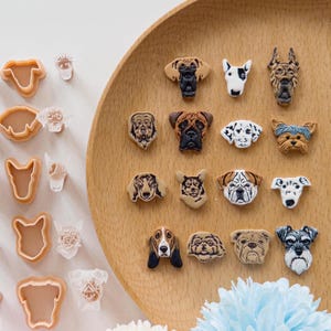 May include: A collection of dog-themed embellishments, including various breeds, arranged on a wooden tray. The embellishments feature detailed facial features and come in a variety of colors, including brown, black, and white. Some are in the shape of a dog's head, while others are cookie cutters.