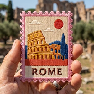May include: A rectangular embroidered patch shaped like a postage stamp with a pink scalloped border. The design features the Colosseum in yellow and brown, a tall blue cypress tree, a red sun, and white clouds against a beige background. The word ROME is stitched in brown letters at the bottom.