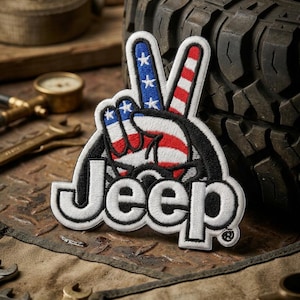 May include: Embroidered patch featuring a peace sign with the American flag design. The word "Jeep" is embroidered in white. The patch is set against a backdrop of a tire and tools.