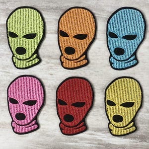May include: Six embroidered patches in the shape of a ski mask. The patches are in various colors: yellow-green, orange, light blue, pink, red, and yellow. Each mask has black eye and mouth openings.
