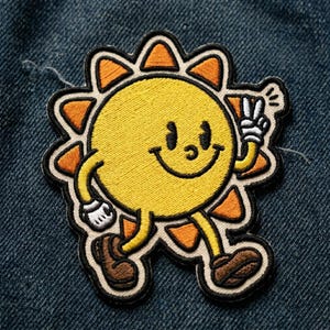 May include: Embroidered patch featuring a smiling yellow sun character with orange rays, black eyes, and a peace sign. The sun has brown shoes and white gloves. The patch is on a blue denim background.
