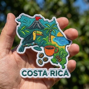 May include: An embroidered patch shaped like the map of Costa Rica, featuring a toucan, a volcano with a red top, a palm tree, a blue body of water, an orange coffee cup, and coffee beans. The text COSTA RICA is embroidered in green at the bottom.