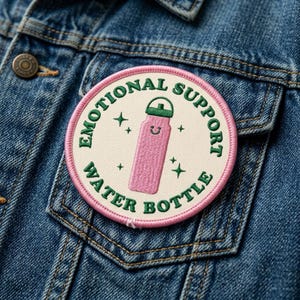 May include: Embroidered patch with the words "EMOTIONAL SUPPORT WATER BOTTLE" in green around a pink water bottle illustration. The patch is circular with a pink border and is attached to a denim jacket.