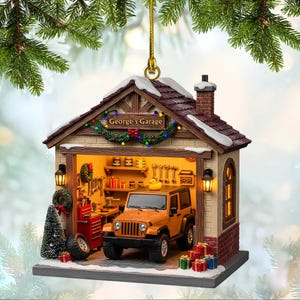 May include: A Christmas ornament shaped like a garage with the text "George's Garage". The garage features a small orange Jeep, tools, and a Christmas wreath. The roof is covered in snow, and the ornament is decorated with Christmas lights.