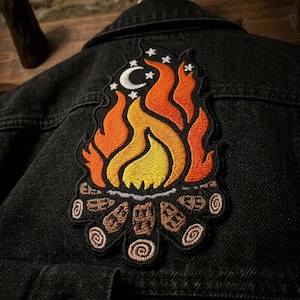 May include: A white ceramic mug with a black handle and the text "But First, Coffee" in a bold, black font. The mug is set against a blurred background, suggesting a cozy setting.