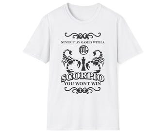 May include: White t-shirt with a black graphic design featuring two scorpions flanking a chess piece. The text reads "NEVER PLAY GAMES WITH A SCORPIO YOU WON'T WIN."