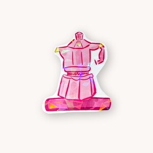 May include: A pink sticker of a stovetop espresso maker. The sticker has a holographic effect, with a geometric base and a detailed outline of the coffee pot. The design is a vibrant pink with yellow and orange accents.