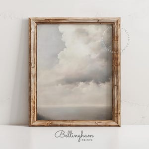 May include: A framed print featuring a serene landscape with a cloudy sky and a calm sea. The artwork is in muted tones of gray, white, and beige, and is enclosed in a rustic, light brown wooden frame. The print is labeled "Bellingham Prints".
