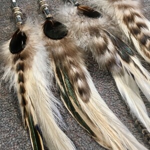 May include: Five white and brown feathers with black tips and green accents are tied together with white string and silver beads.