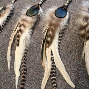 May include: Three feather hair ties with silver beads and black and white feathers. The feathers are arranged in a fan shape and have a blue accent.