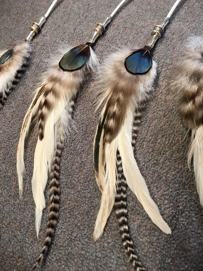 May include: Three feather hair ties with silver beads and black and white feathers. The feathers are arranged in a fan shape and have a blue accent.