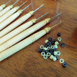 May include: A set of eight wooden crochet hooks with gold tips and a pile of black and beige micro rings for hair extensions.