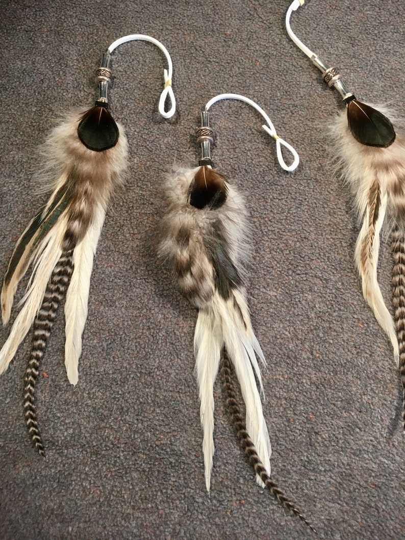 May include: Three feather dreamcatchers with white and brown feathers, black and green accents, and silver beads. The dreamcatchers are hanging from white cords.