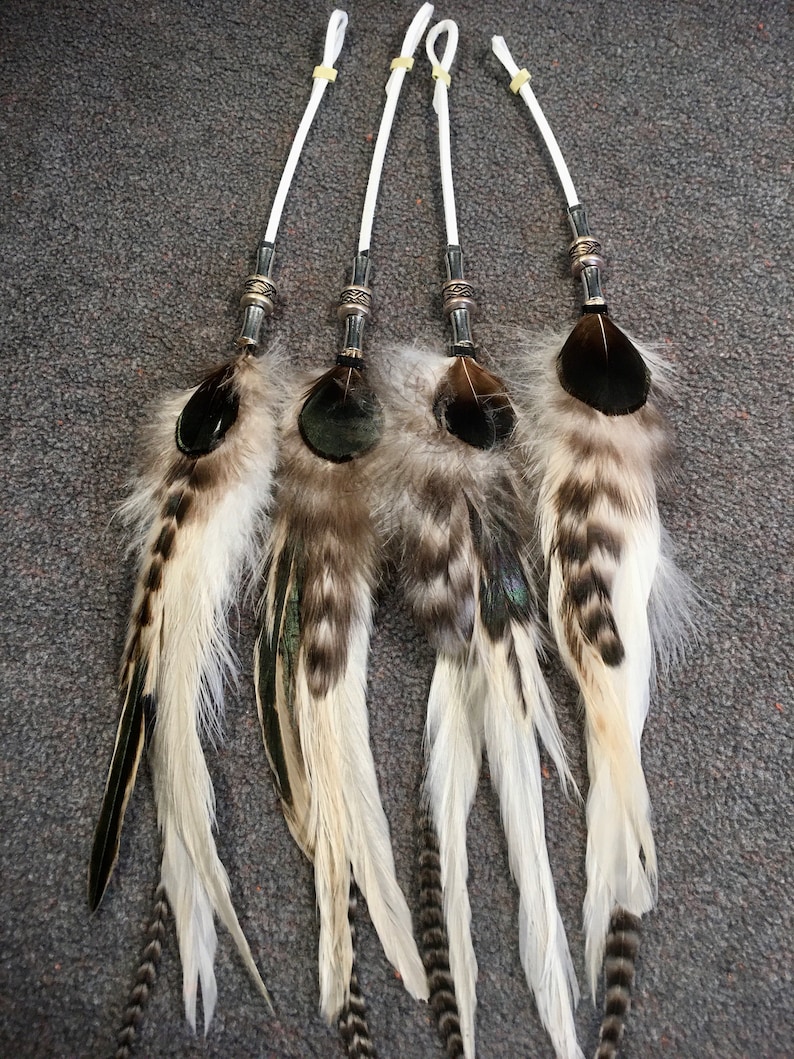 May include: Four white feather hair ties with black and brown accents. Each tie has a silver metal bead and a white string.