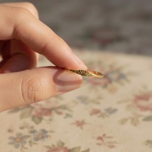 Peut inclure: Une bague dorée avec un motif de soleil. La bague est tenue entre les doigts, mettant en valeur les détails délicats. Le design de la bague présente un motif de soleil, ajoutant une touche d'élégance. La bague est un bijou.
