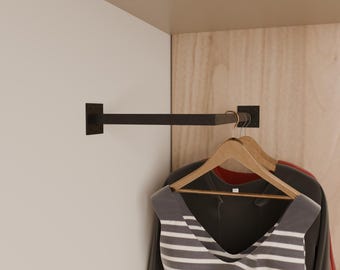 May include: A dark brown metal clothing rail fixed to a white wall. Several wooden coat hangers with clothes are suspended from the rail. The clothes include a striped vest and a dark grey top.