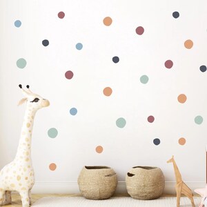 May include: A white wall adorned with colorful polka dot wall decals in shades of blue, orange, green, and burgundy. A giraffe figurine and woven baskets are in the foreground, suggesting a nursery or playroom theme.